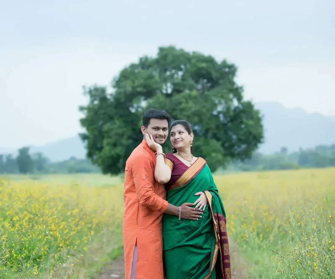 An expecting couple stands together in a vast field of yellow wildflowers, dressed in beautiful traditional Indian attire. This outdoor maternity portrait captures a serene and classic pose, highlighting their bond against a natural, picturesque backdrop.
