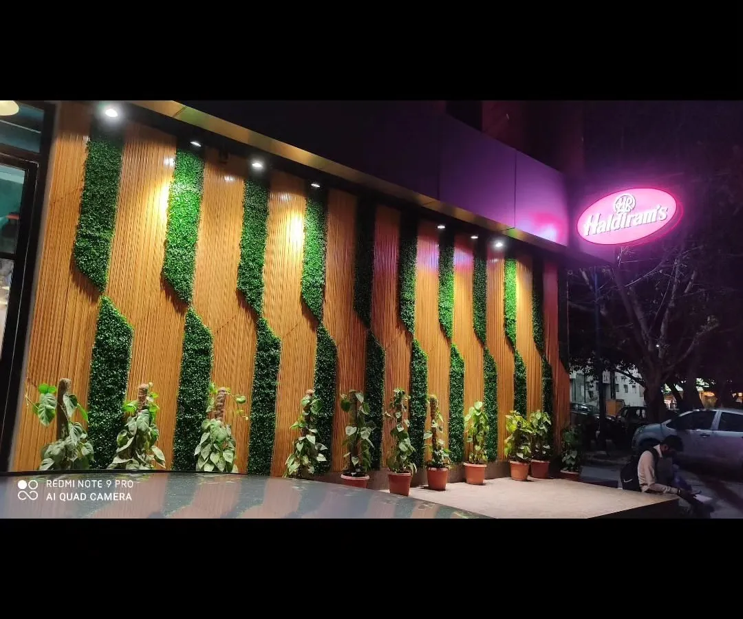 For commercial clients, I create eye-catching facades that attract customers. Here is an installation for a Haldiram's outlet, where I integrated vertical green panels with wood-style slats for a bold, branded exterior.