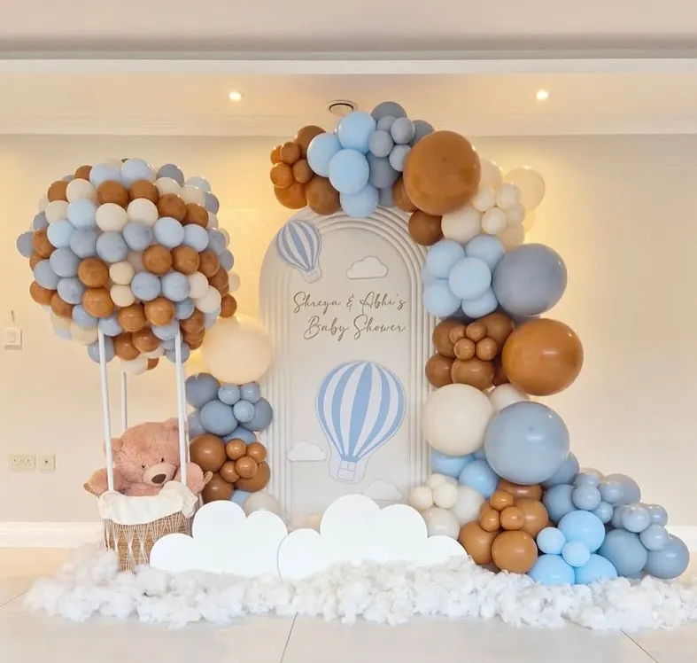 An elaborate 'Up, Up and Away' hot air balloon themed baby shower. This setup includes a large balloon sculpture forming a hot air balloon with a basket for a teddy bear, set against a custom backdrop and surrounded by clouds of balloons.