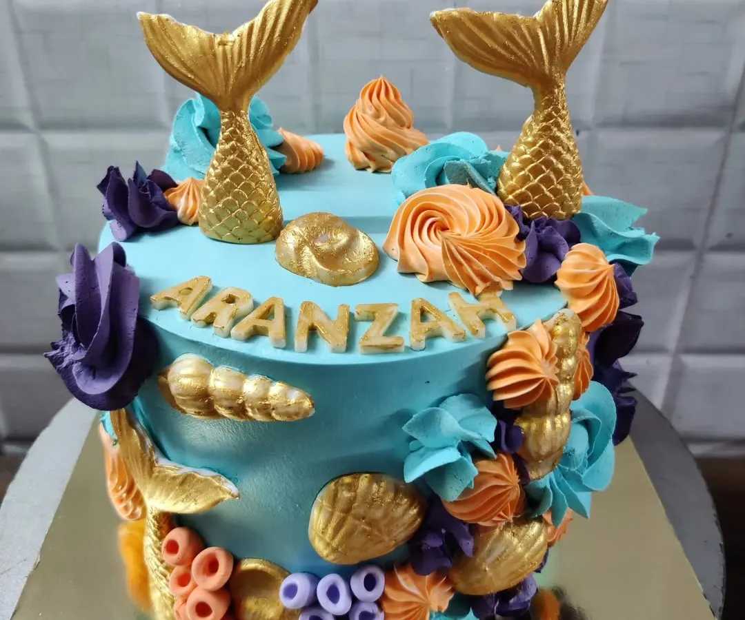 An enchanting mermaid-themed cake perfect for a magical birthday. This custom cake is decorated with golden mermaid tails, colorful buttercream corals, and delicate seashells.