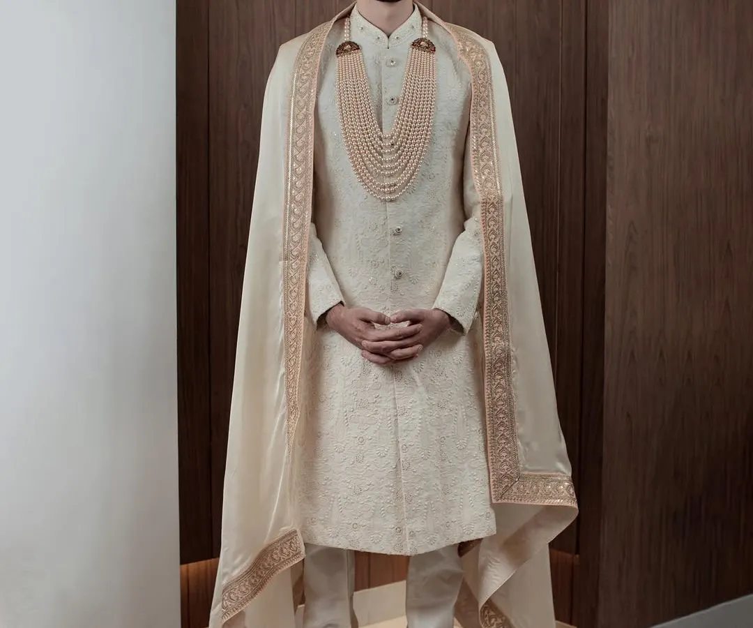 For the groom who desires nothing less than royalty. This ivory sherwani, complete with a regal cape and a multi-layered pearl necklace, is designed to make a grand statement on your most important day.