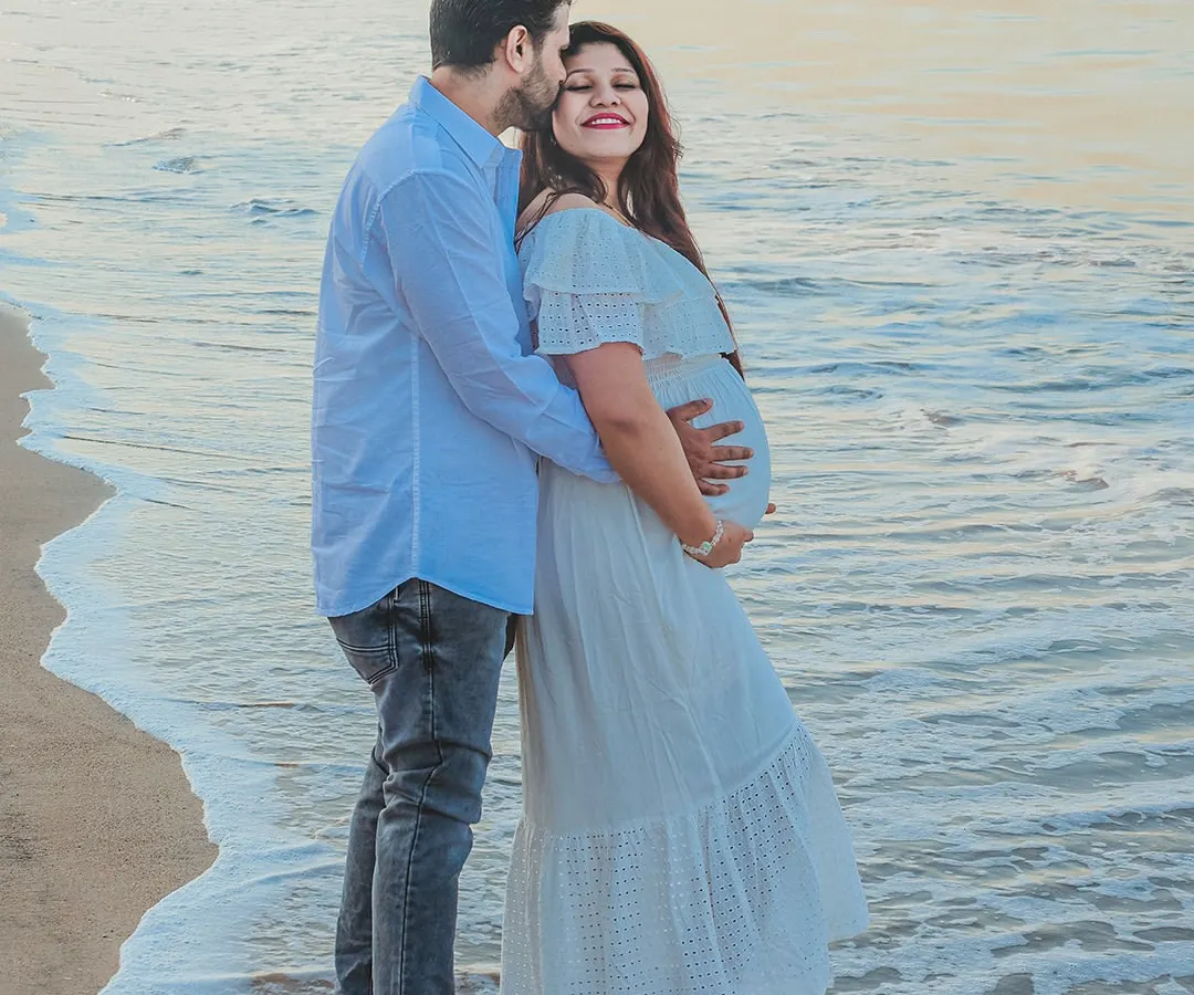 An outdoor maternity photoshoot at the beach, capturing a quiet moment between the expecting couple. The soft evening light and gentle waves create a serene and romantic backdrop for your pregnancy portraits.