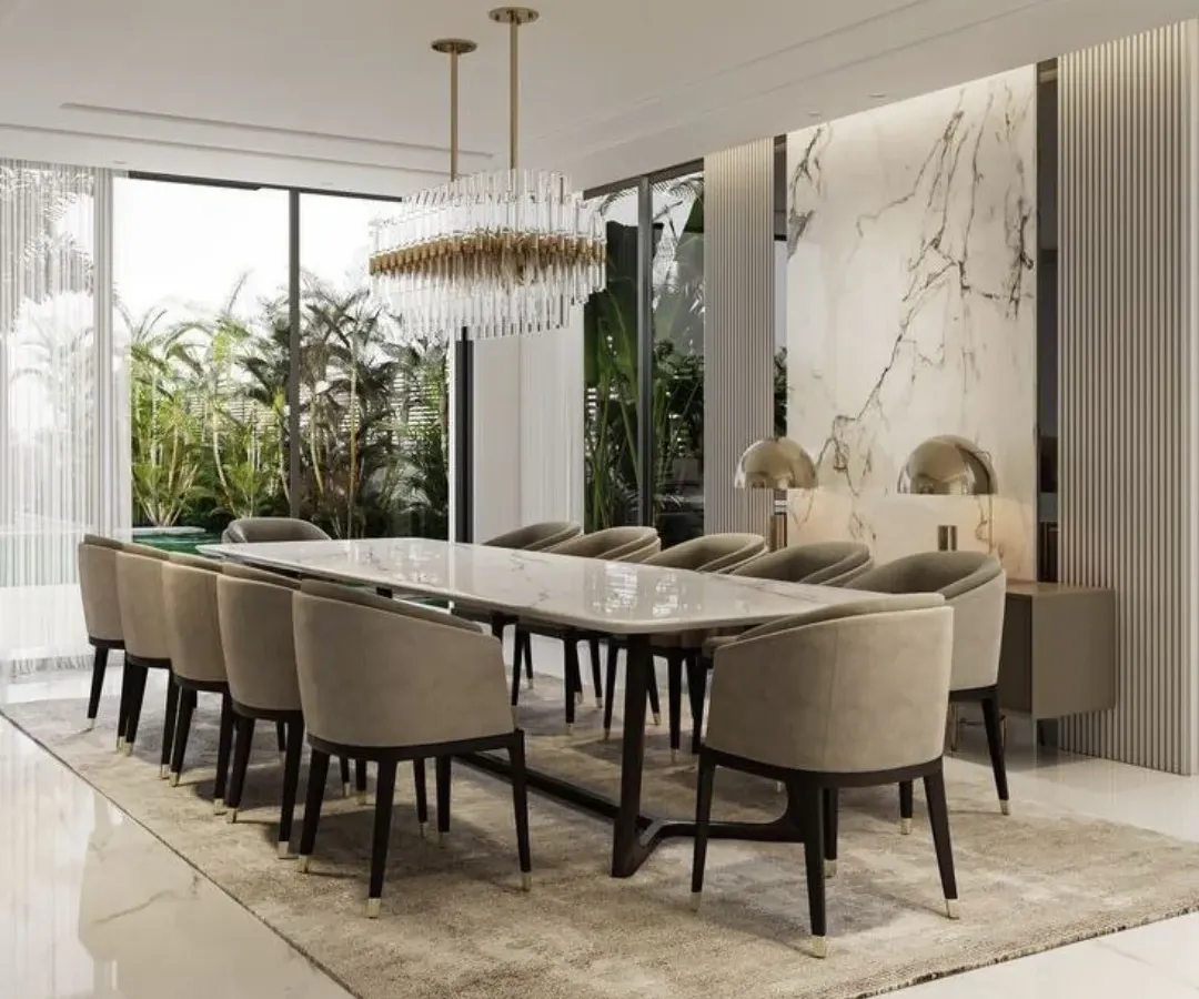 We designed this expansive dining room for elegant entertaining, featuring a ten-seater marble-top table and plush upholstered chairs. A dramatic crystal chandelier hangs above, while the marble accent wall and large windows create a bright, sophisticated atmosphere perfect for hosting memorable dinners.