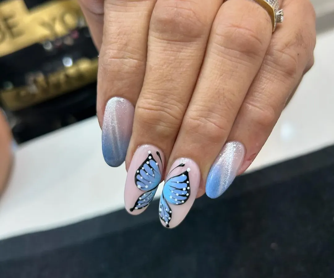 Let your nails take flight with our custom hand-painted butterfly art. This detailed design is set against a beautiful blue ombré and cat eye background, showing the delicate and artistic work our nail technicians are capable of.