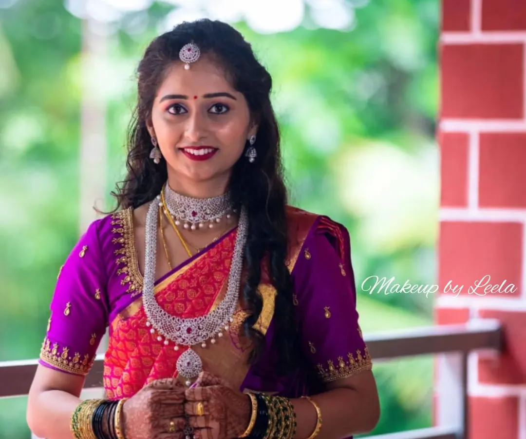 This is a perfect example of a modern reception look. The client is wearing a vibrant pink and purple Kanjeevaram saree with elegant diamond jewelry. Her makeup is glamorous yet sophisticated, with soft, flowing curls completing the style.