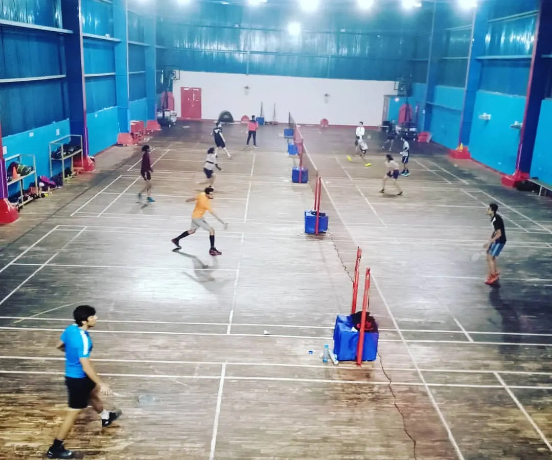 A wide view of our bustling indoor badminton academy during a group training session. Multiple courts are active with players engaged in various drills, showcasing our capacity to train numerous athletes simultaneously.