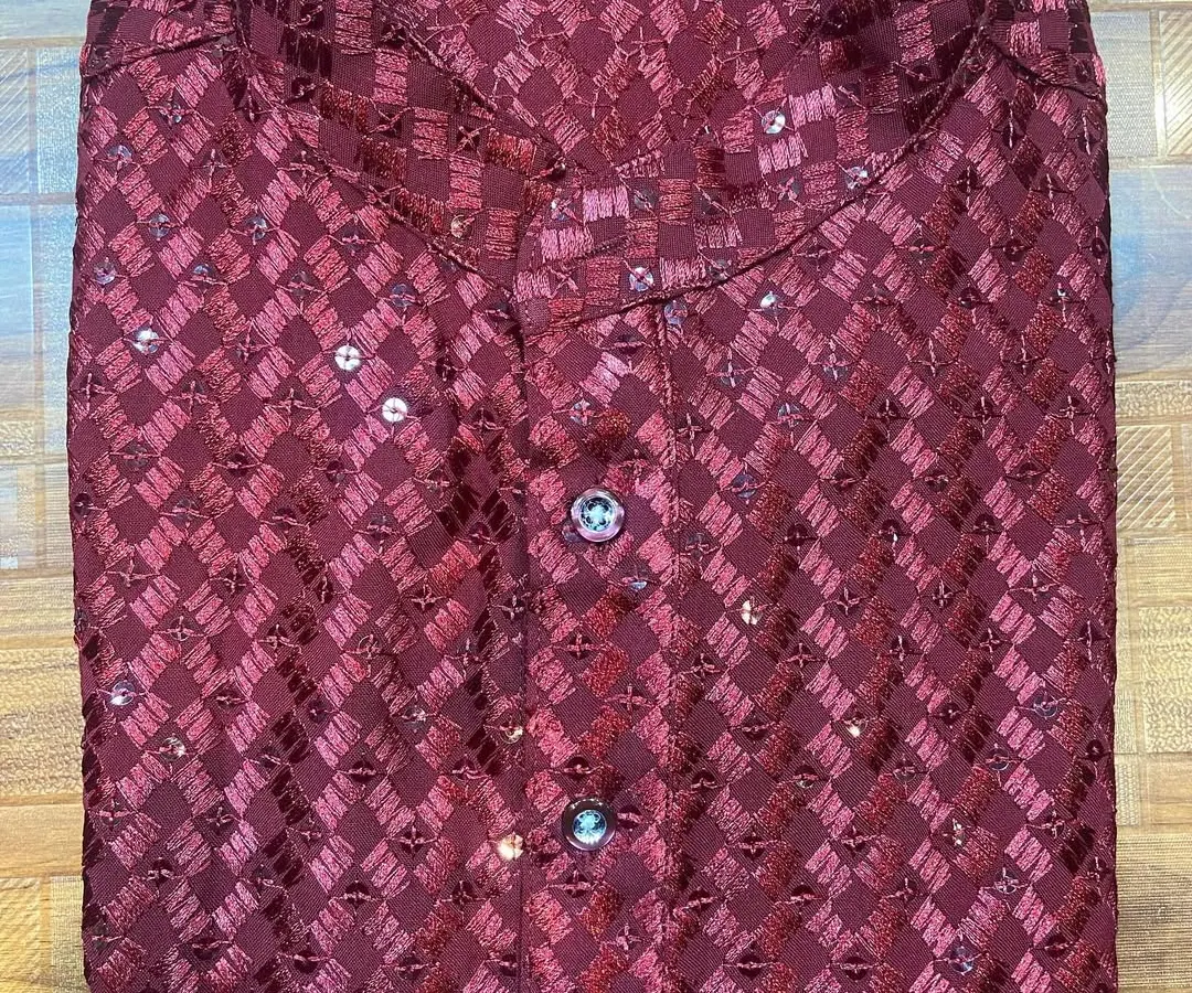 A folded view of a festive men's kurta in a rich maroon, made from a patterned fabric with delicate sequin work. This piece highlights the kind of detailed craftsmanship available for special occasions like Diwali or sangeet ceremonies.