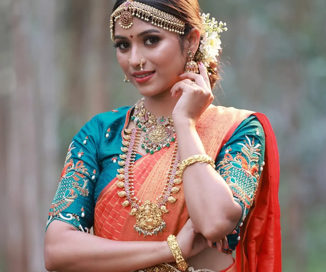 I love capturing the timeless grace of a traditional bridal look. This outdoor shoot focused on the intricate details of the temple jewellery and the rich texture of the orange and teal silk saree against a natural, wooded backdrop.