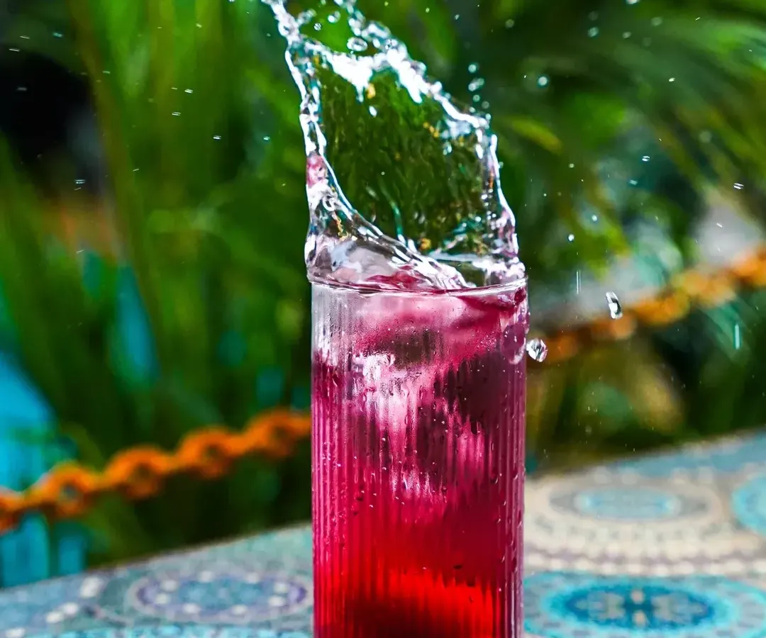 A dynamic action shot capturing the perfect splash in a vibrant red cocktail against a lush green background. This kind of high-speed beverage photography is ideal for creating exciting visuals for bar menus and social media campaigns.