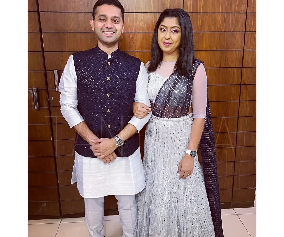 I love creating coordinated looks for couples. Here, we have a custom-made embellished Bundi jacket and raw silk kurta set for him, perfectly complementing her stunning glitter net fish-cut lehenga with an attached dupatta.