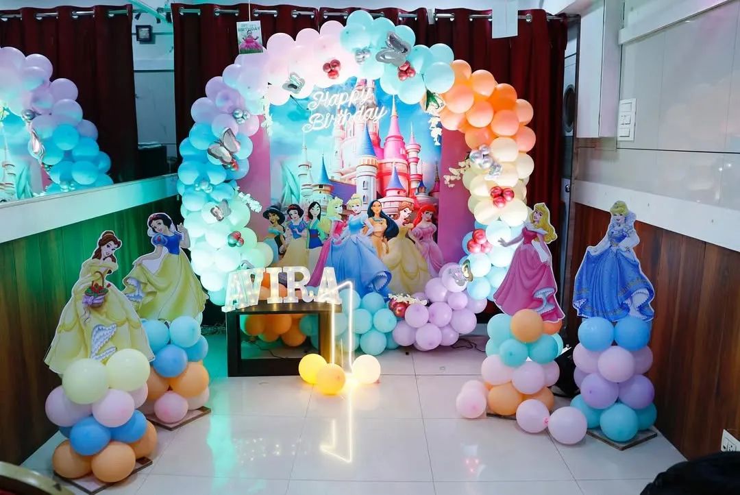 A magical Disney Princess theme for a first birthday. This enchanting setup features a pastel rainbow balloon arch, a castle backdrop, and life-sized cutouts of Cinderella, Snow White, and other princesses, creating a fairytale experience.