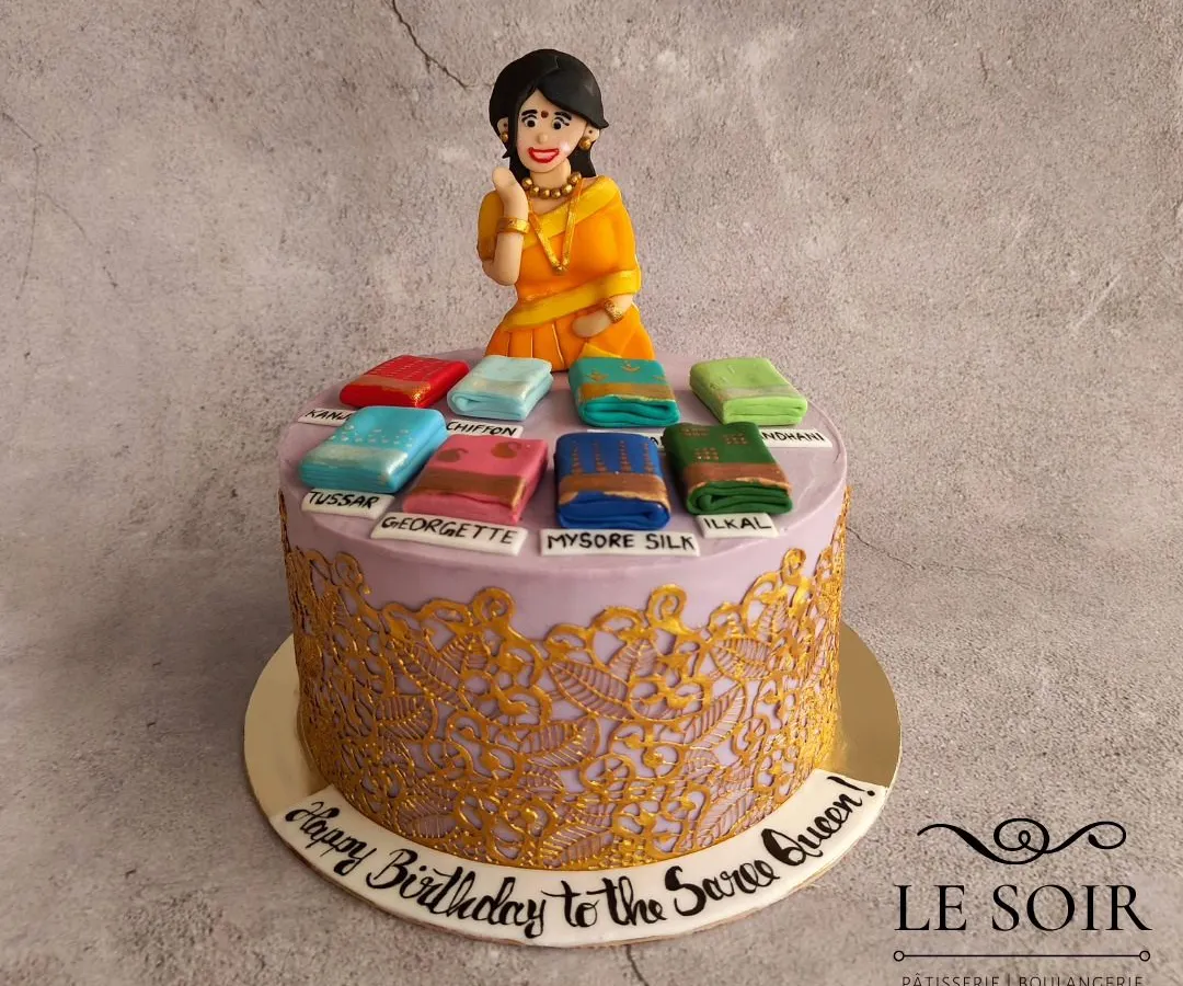 I love bringing your passions to life, like with this "Saree Queen" cake. It features a hand-sculpted figurine and a collection of miniature, detailed 3D sarees in various styles like Mysore Silk and Georgette, all sitting on a cake with an intricate golden lace design.