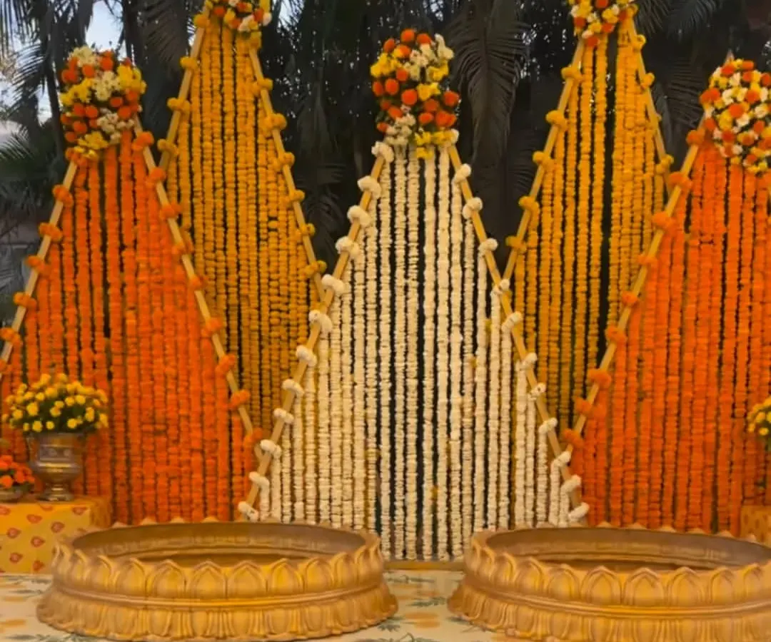 For this haldi ceremony at a farmhouse, I created a unique backdrop with triangular panels made entirely of fresh marigold and tuberose strings. The two golden urlis in the front are ready for the ceremony's rituals.