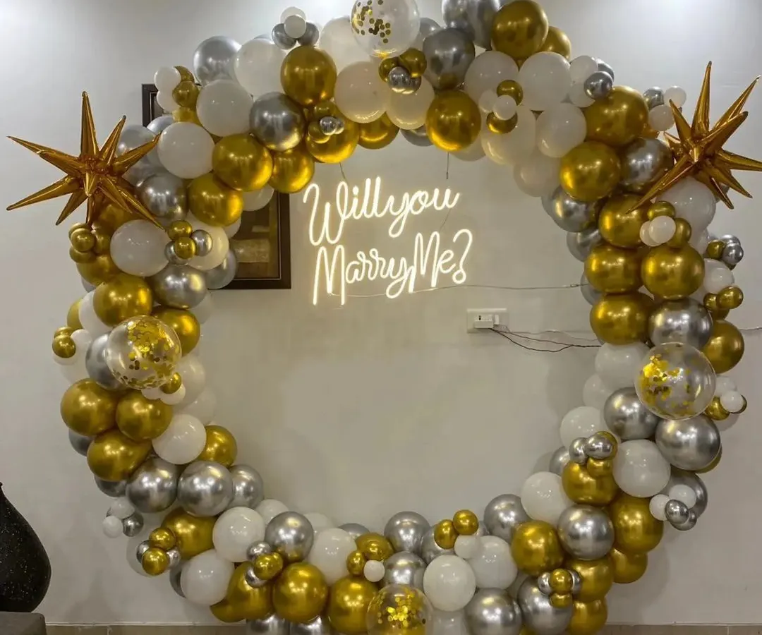 For that unforgettable moment, I design stunning proposal backdrops. This setup features a large ring decorated with gold, silver, and white balloons, with a "Will you Marry Me?" neon sign to make the question pop.