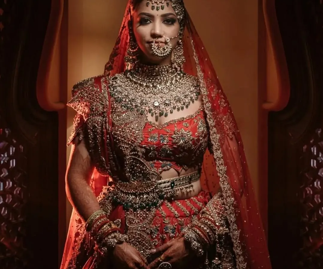 A full-length bridal portrait showcasing the magnificent red lehenga and intricate jewelry. We use careful lighting to make sure every detail of the bride's look is captured perfectly.