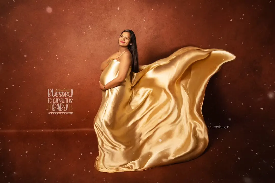 A truly glamorous maternity portrait featuring a solo mom-to-be. The flowing golden satin fabric creates a sense of movement and elegance, making for a dramatic and unforgettable fine-art pregnancy photo.