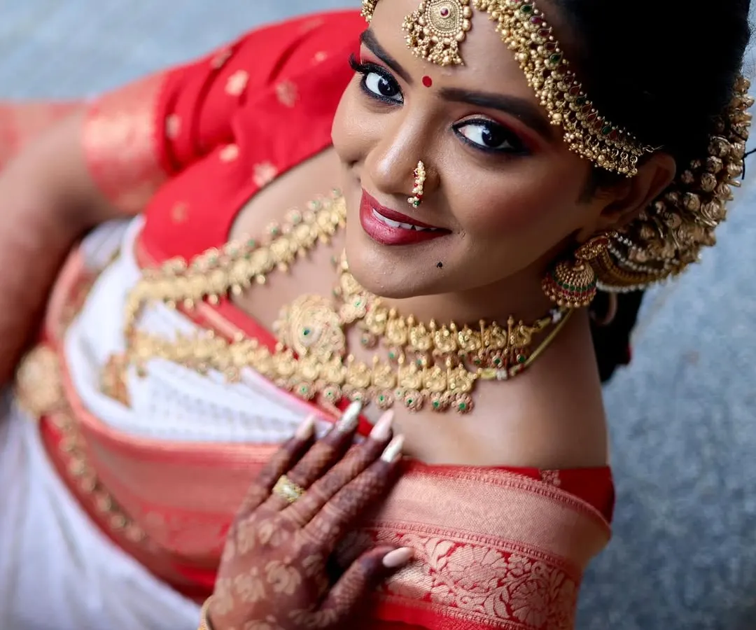 A beautiful high-angle shot of a South Indian bride in her traditional red and white saree. This perspective highlights the stunning temple jewelry and the elegance of the moment.