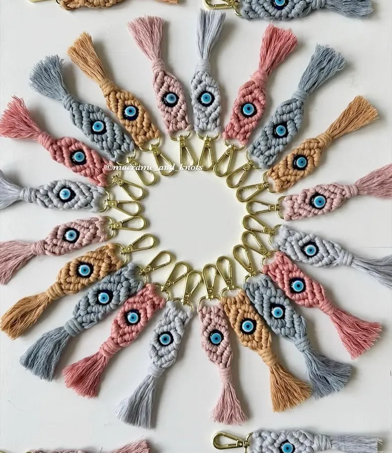 My handmade evil eye keychains are one of my most loved items, especially for gifting. This photo shows a large custom order with a mix of dusty pink, grey, and tan cotton cords, each with a protective evil eye bead at its center.