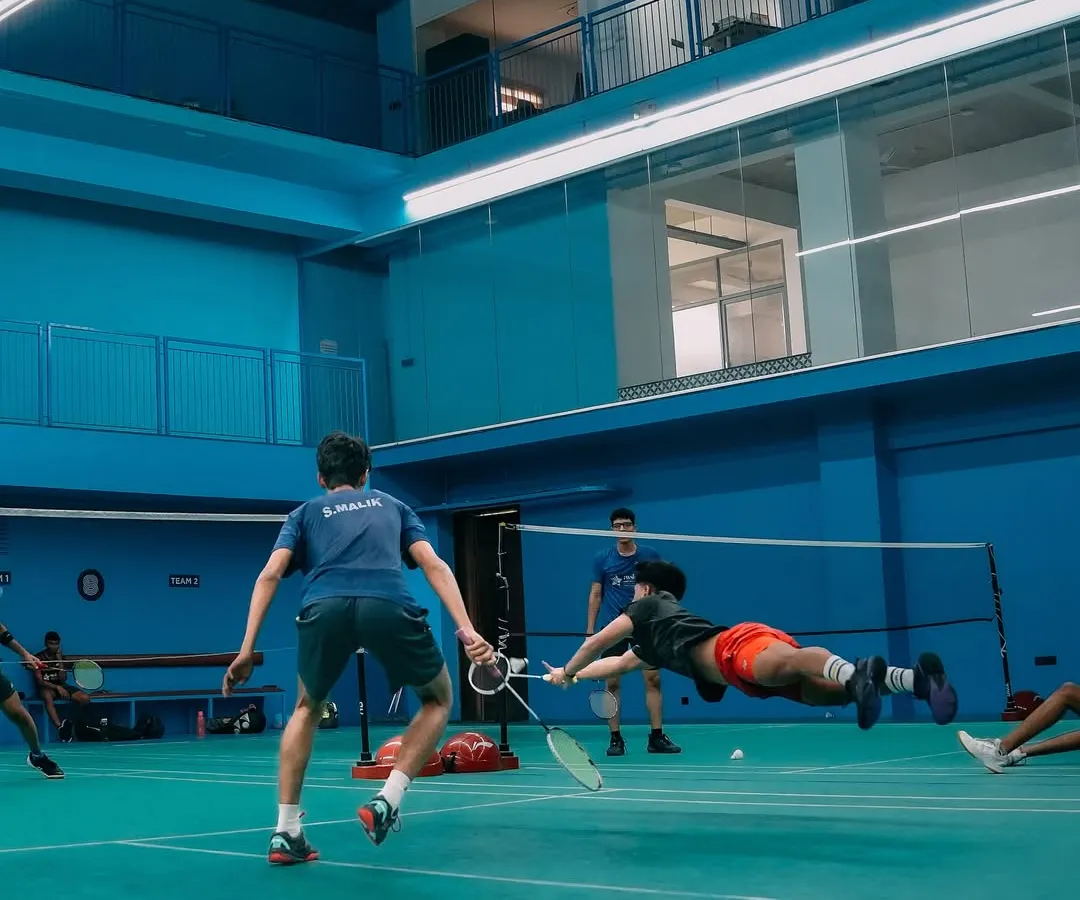 This is what dedication looks like. A player diving with full commitment during an intense badminton training session, capturing the high-energy atmosphere of our courts.