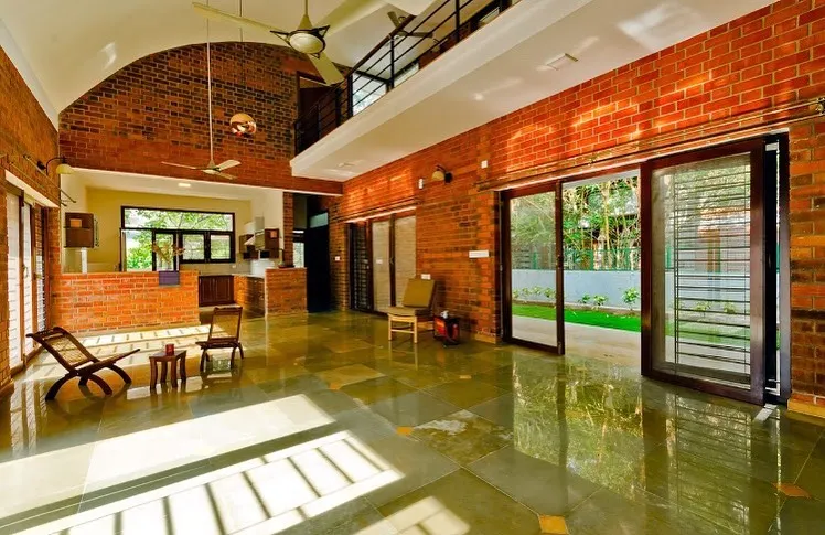 The interior of the Vidyut Kapoor Residence reveals a double-height living space, a signature element in our designs. This feature, combined with expansive glass doors and exposed brick walls, creates an airy, light-filled home that seamlessly connects to the surrounding green space.