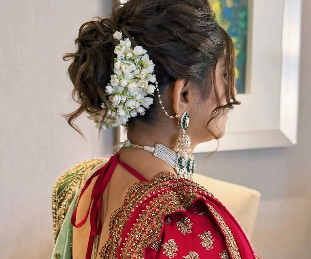 A detailed view of a traditional bridal updo, intricately woven and adorned with fresh jasmine flowers, or gajra. This classic hairstyle is perfect for wedding ceremonies, offering a timeless elegance that complements traditional Indian bridal wear.
