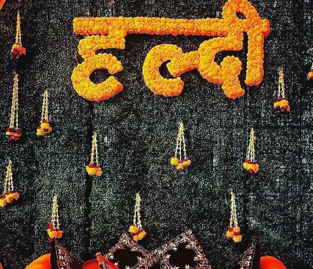 This is a close-up of our signature Haldi ceremony backdrop, a highly requested design for its traditional beauty. We crafted the word "Haldi" in Hindi using dense, fresh marigold flowers, set against a dark green foliage wall. The design is completed with delicate hanging floral tassels, creating a rich, textured look that is perfect for photos.
