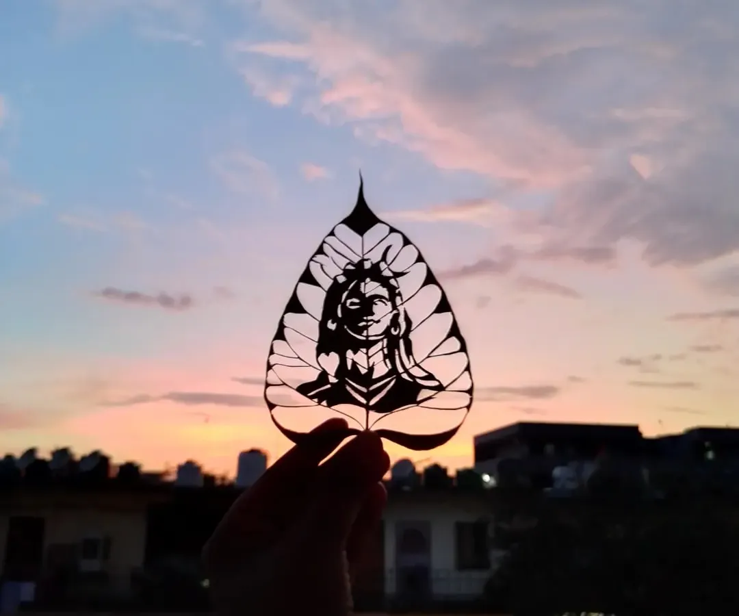 Here is one of my favorite leaf carvings, an image of Adi Yogi. I held it up to the sunset to show how the light passes through the delicate cuts, making the art glow. This is the magic of leaf art.
