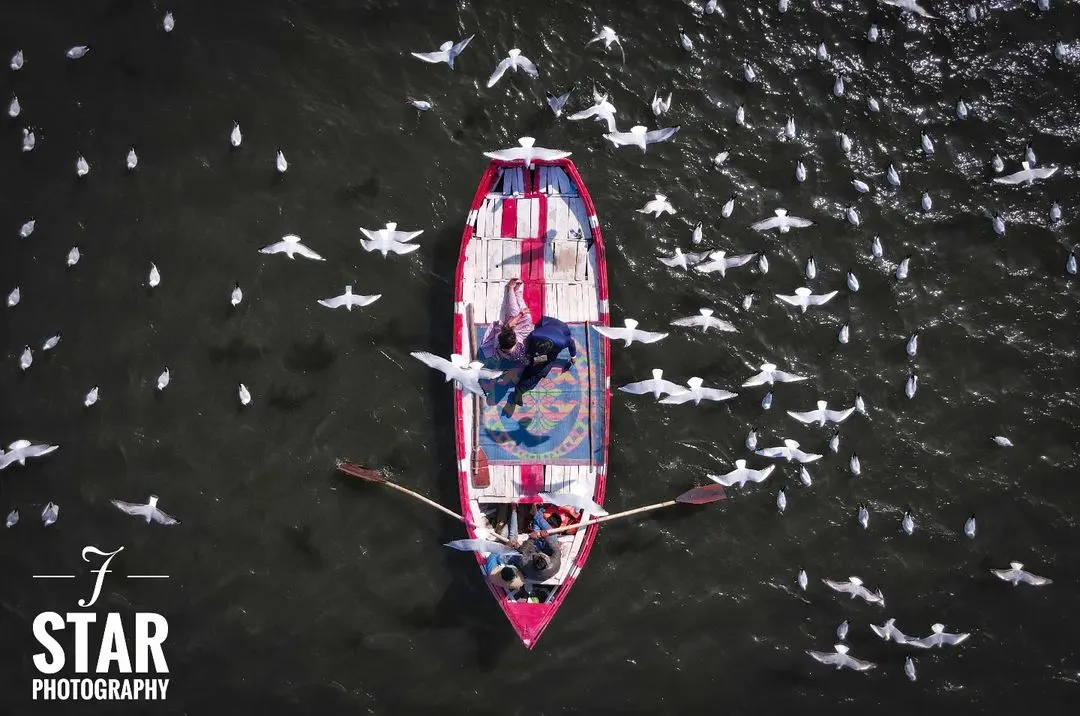 A top-down drone view of a couple's pre-wedding shoot at the Sangam in Prayagraj, surrounded by birds. This unique aerial perspective creates a truly memorable and artistic photograph.