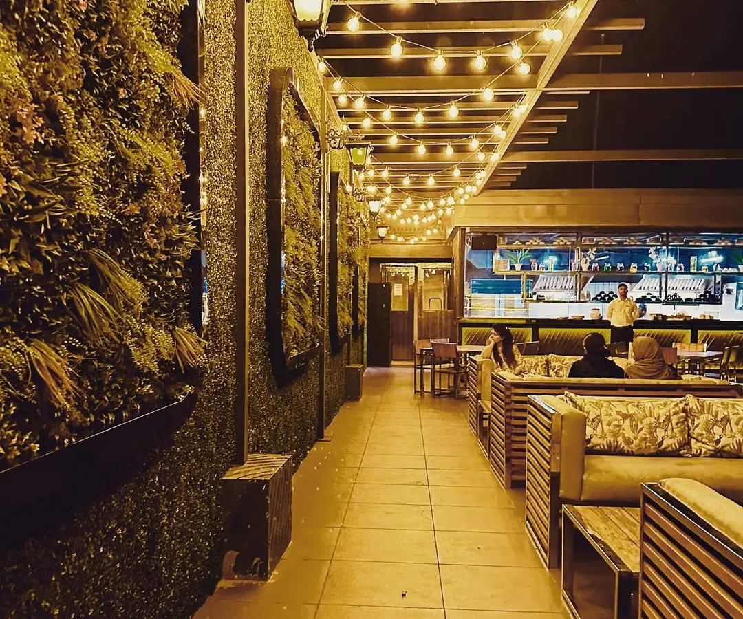 We designed this rooftop cafe to create an inviting atmosphere for evening patrons. The combination of a vertical green wall, warm string lights under the pergola, and comfortable slatted wood furniture provides a perfect example of our commercial landscape and lighting design services.