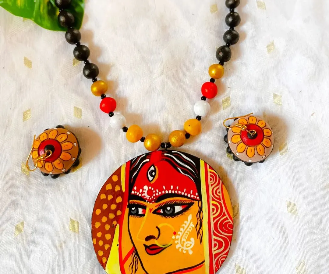 I pour my heart and devotion into these hand-painted pendants. This piece features the serene face of a goddess, detailed with traditional motifs, making it perfect for festive occasions or as a piece of wearable art. The necklace is strung with terracotta beads that complement the pendant.