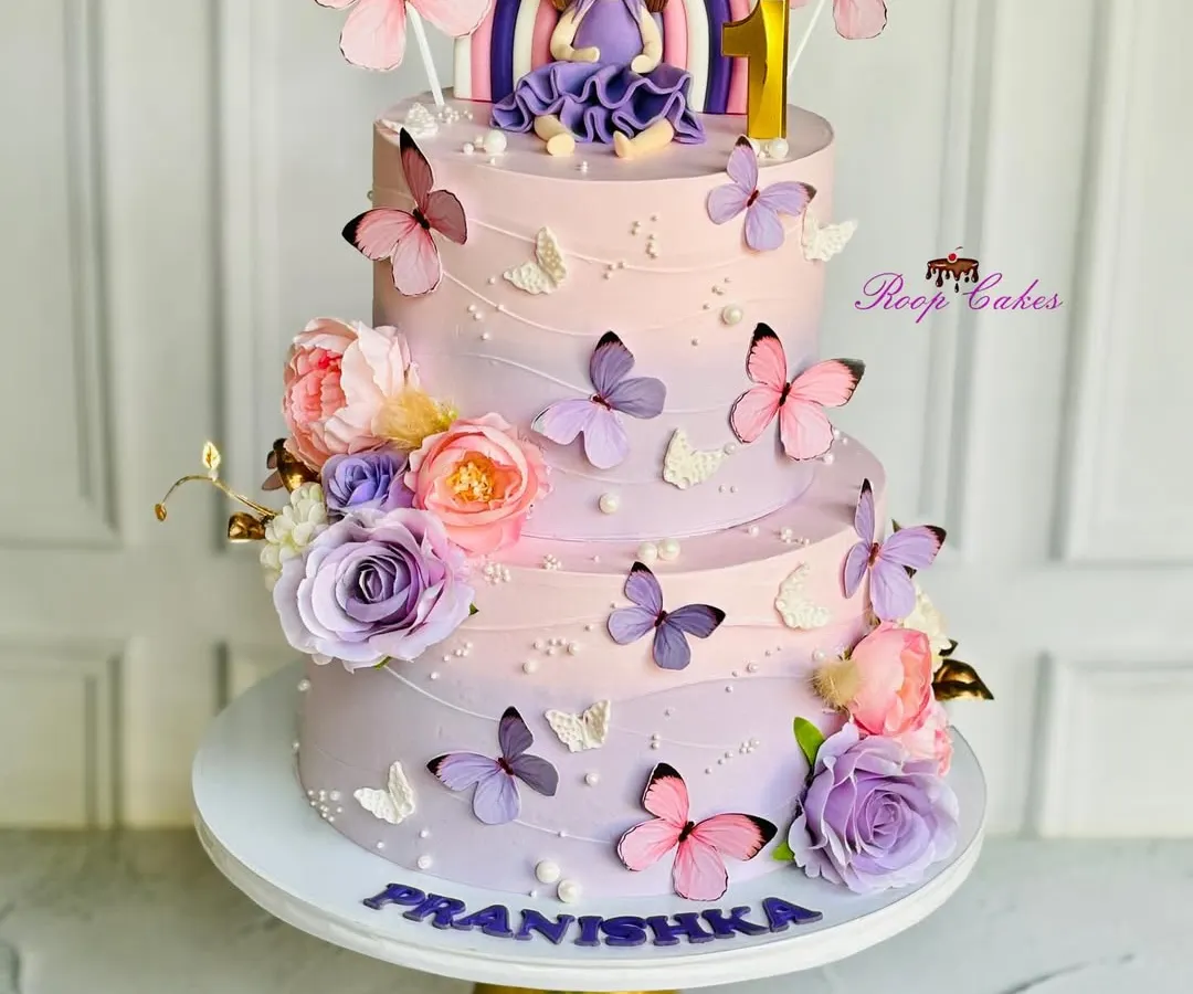 A magical two-tier cake for a very special first birthday. This design features a beautiful lavender and pink ombre effect, a custom fondant doll, and delicate butterflies, all coming together to create a fairytale celebration.