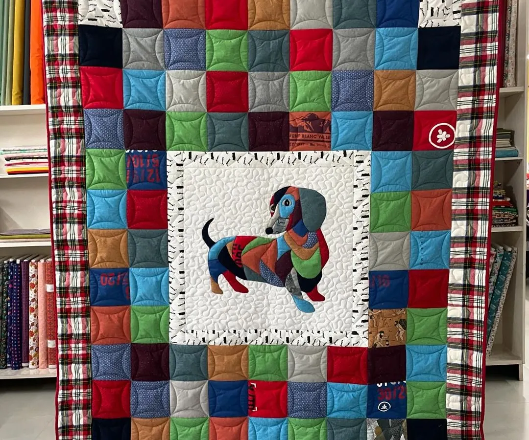 We love bringing memories to life. This T-shirt memory quilt, featuring a custom dachshund appliqué, was created for a client's son, transforming his cherished shirts into a cozy and personal keepsake.