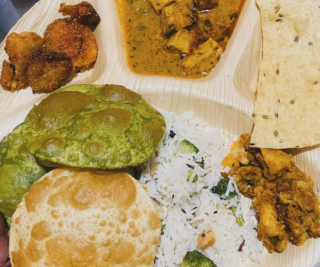 A look at our complete homestyle thali. This one features fluffy pooris, including a vibrant palak poori, served with paneer curry, vegetable rice, a dry vegetable side, papad, and fried potatoes.