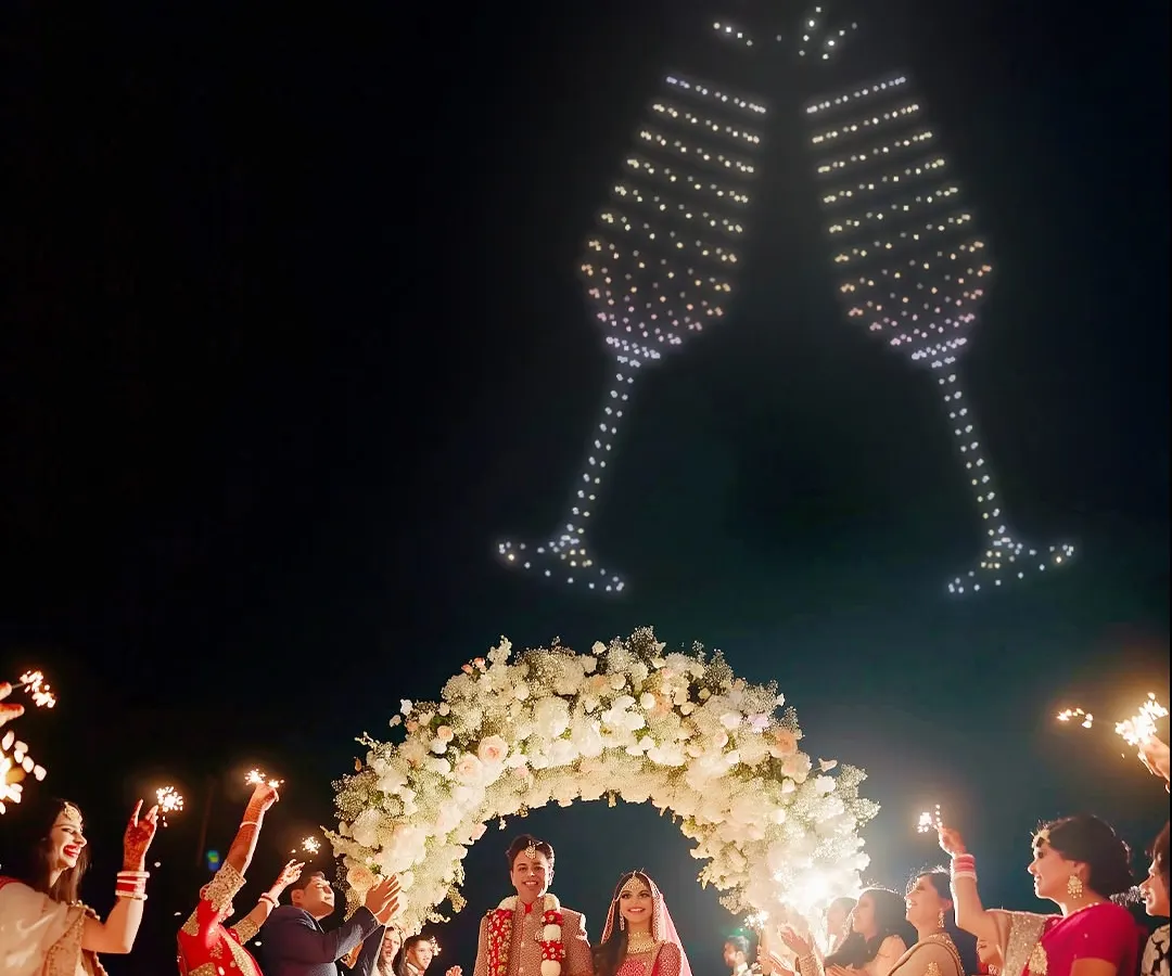 Let's toast to your new beginning in the grandest way possible. Here, I've created giant, clinking champagne glasses in the sky, perfectly timed to celebrate the couple's union as their guests cheer them on with sparklers.