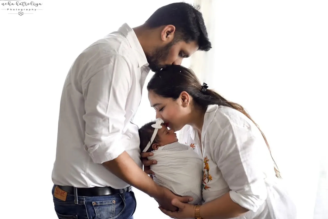 The first family portrait is always so special. Here, both parents share a gentle kiss with their newborn, creating a beautiful memory of their first days together, all dressed in classic, simple white.