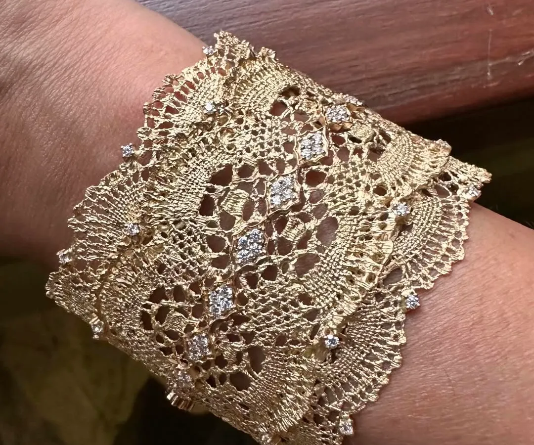 A close-up view of my signature lace cuff, worn on the wrist. This piece is inspired by delicate Chantilly lace and is meticulously hand-woven from 18k yellow gold, with natural diamonds scattered like dewdrops to catch the light.