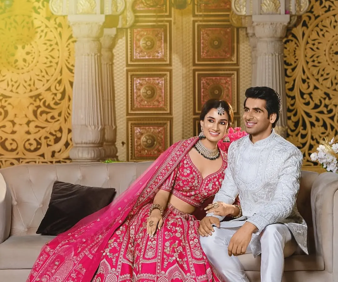 This is a perfect example of coordinated styling for a modern reception or engagement. The bride's vibrant pink lehenga is intricately detailed, and the groom's elegant white sherwani provides a beautiful contrast, creating a look that is both regal and contemporary.