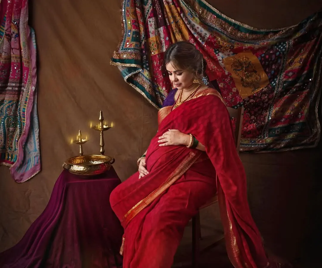 Inspired by the timeless paintings of Raja Ravi Varma, this portrait captures the divine grace of motherhood. The rich red saree, antique brass lamps, and dramatic lighting come together to create a piece of heritage art.