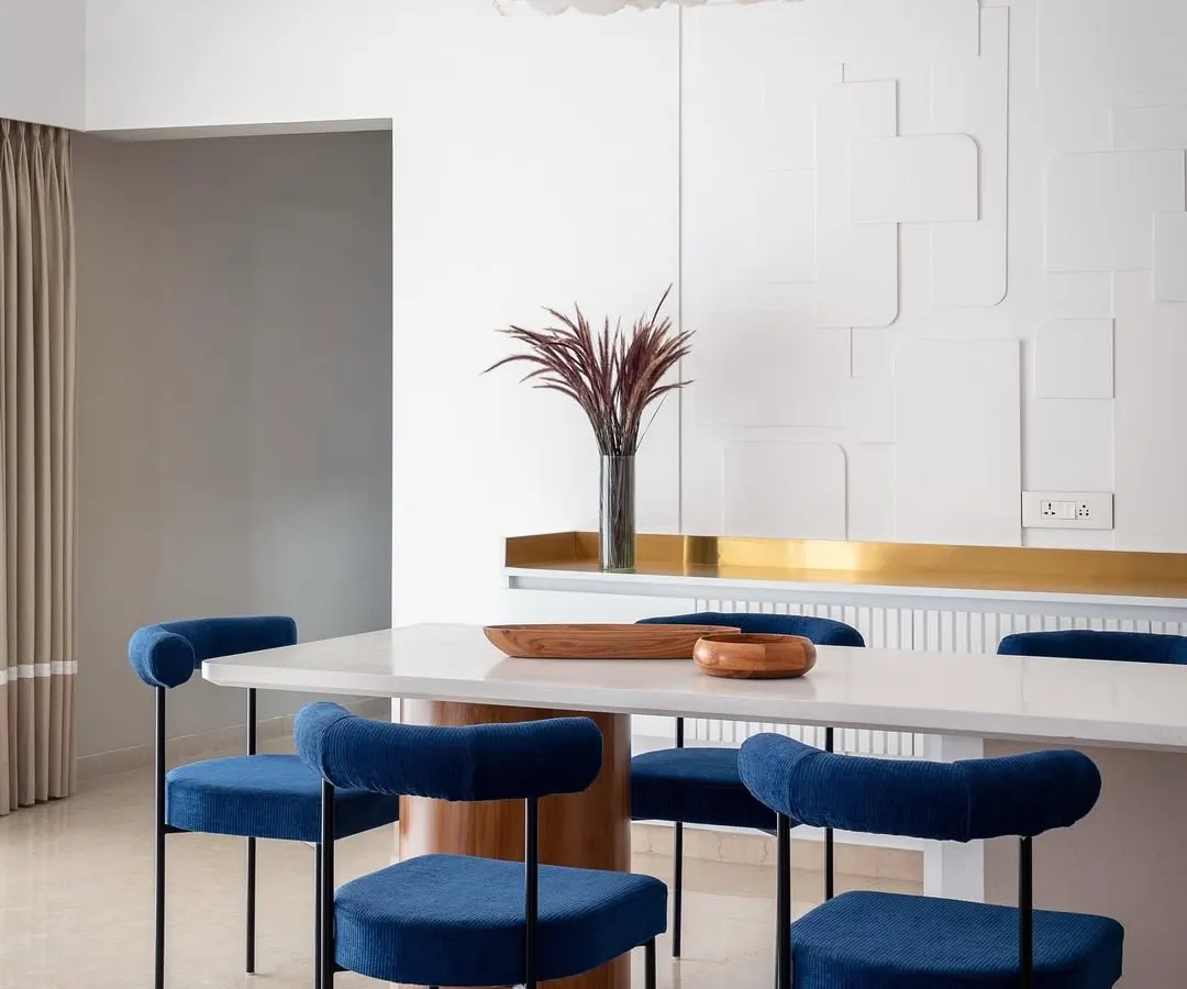 We love adding a pop of color to create drama and personality. In our 'Vishu Home' project, these bold, royal blue velvet chairs stand out against the monolithic white dining table and textured wall, creating a modern yet timeless dining experience that is both elegant and inviting.