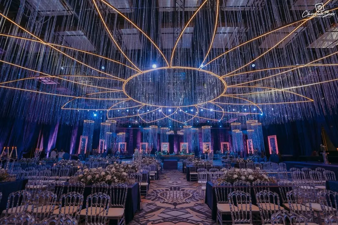 For this sangeet, I envisioned a celestial world. The design is built around dramatic lighting, with a massive, lotus-shaped neon installation and cascading crystal strings that mimic a starry sky. This demonstrates how I use light and structure to transform a large ballroom into an intimate, high-energy environment for celebration.
