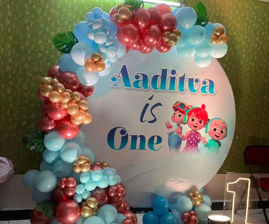 This Cocomelon theme is a favorite for first birthdays. The setup includes a custom circular backdrop with the birthday boy's name, a vibrant balloon garland, and a light-up marquee number '1' to make the milestone special.