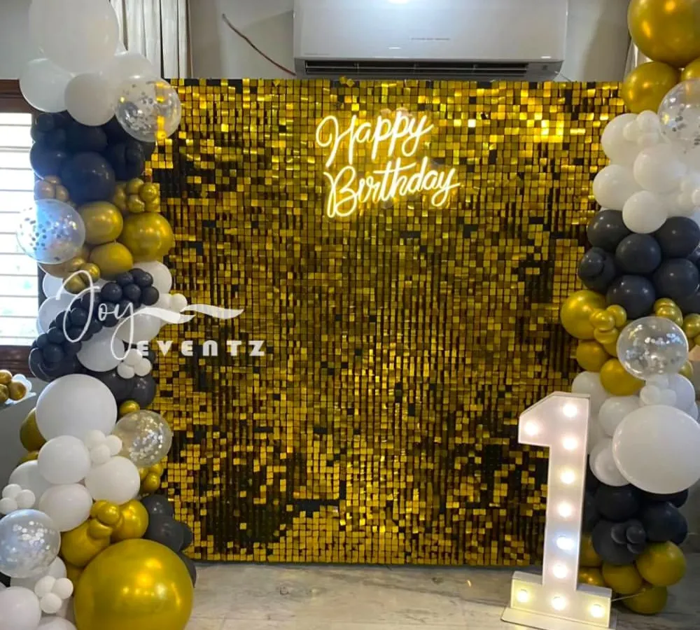 I designed this glamorous and modern birthday backdrop using a gold shimmer wall. The setup is framed by an organic balloon garland in black, white, and gold, and features a 'Happy Birthday' neon sign and a large marquee number '1' to mark the special occasion.