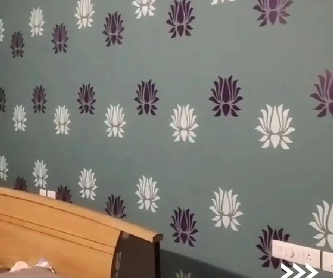 A close-up of a bedroom accent wall featuring a custom two-tone lotus flower stencil. We used a calming sage green base with crisp white and deep purple for the pattern, creating a serene and personalized environment.