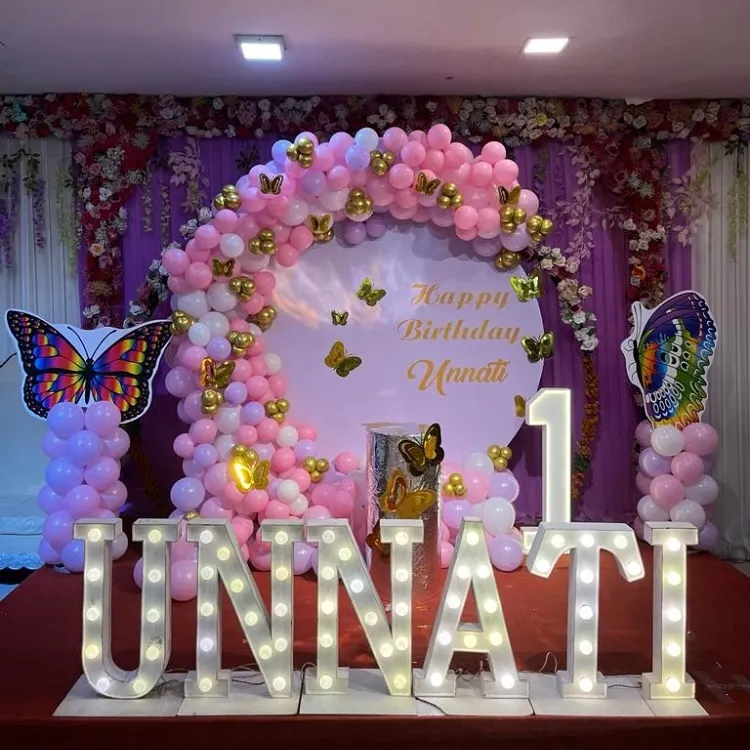 I specialize in creating magical first birthday parties, like this butterfly theme for Unnati. The setup includes a custom circular backdrop, a full balloon arch in pink and gold, and large light-up marquee letters spelling out the name for a perfect photo opportunity.