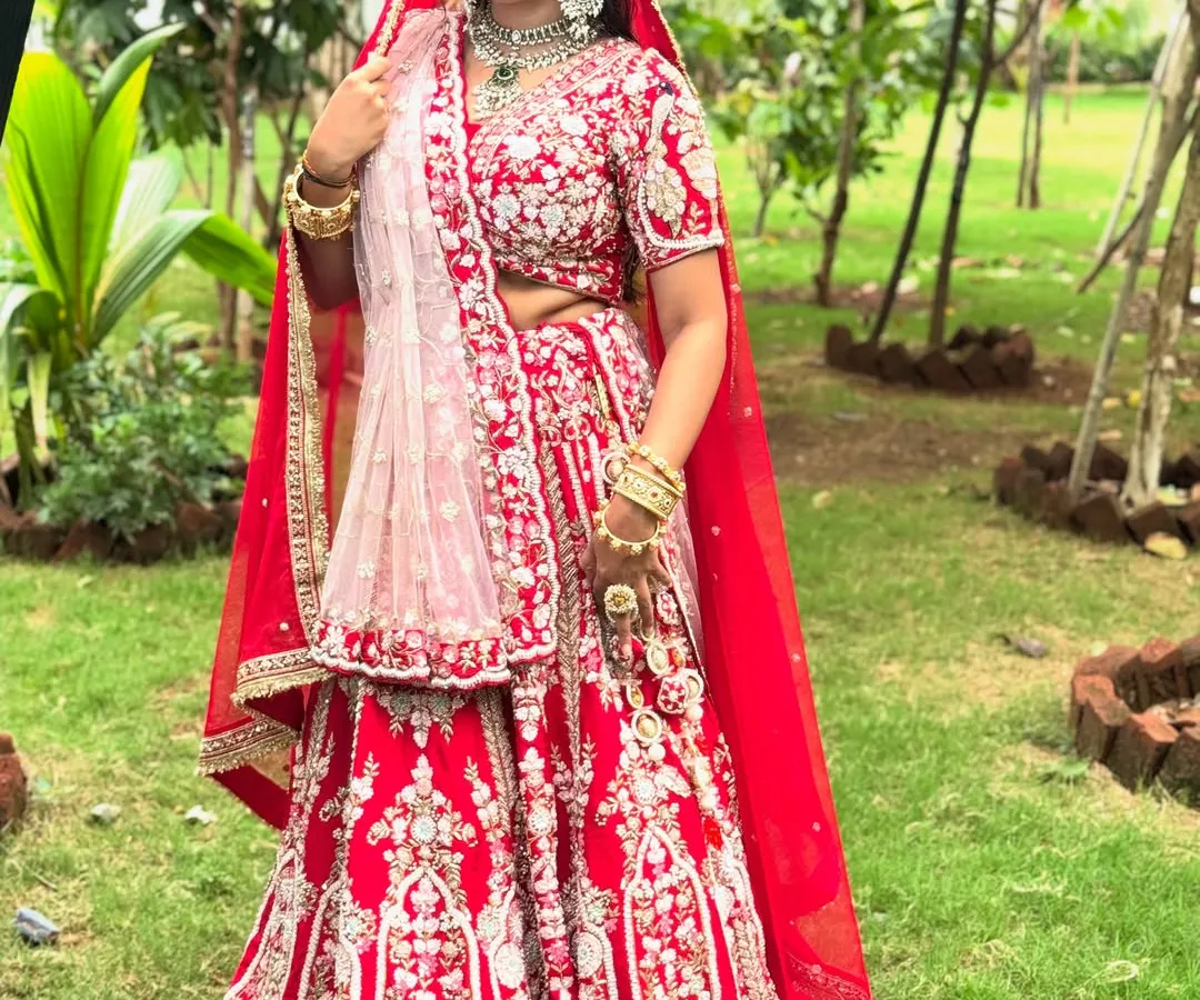 A full view of a classic royal bride in a stunning red lehenga. I provide complete styling, including professional lehenga draping, to ensure every detail is perfect. This look is designed to be grand yet feel comfortable, allowing you to enjoy your day to the fullest.