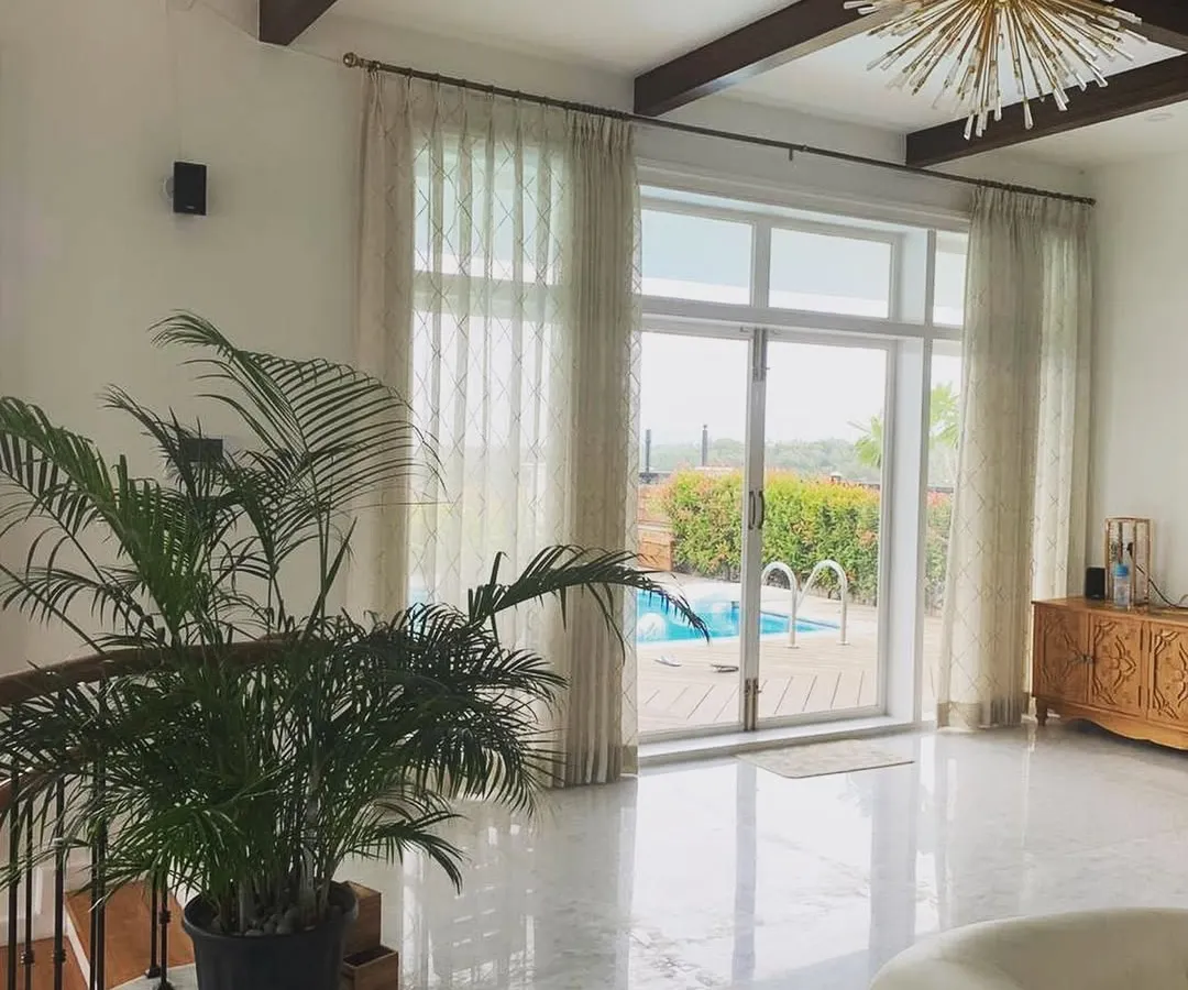 This living space in a Mysore residence for a doctor exemplifies our tropical modernism style. Large glass doors open directly onto a terrace with a swimming pool, creating a seamless flow between the indoor and outdoor areas, complemented by marble floors and natural light.
