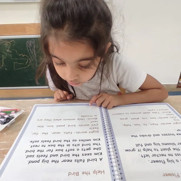I read, I learn. Our literacy program is designed to build a strong foundation, starting with letter sounds and moving towards independent reading. This student is deeply focused on her reading material, a common sight in our K2 program.