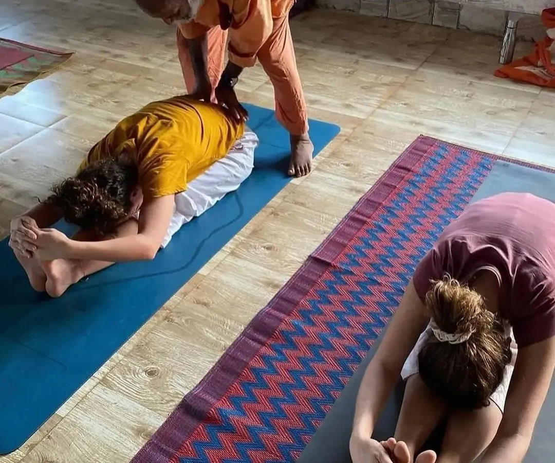In our Hatha yoga sessions, I provide personal guidance to ensure proper alignment and understanding of each asana. Here, I am assisting a student in Paschimottanasana, the seated forward bend, to help them safely deepen the posture.