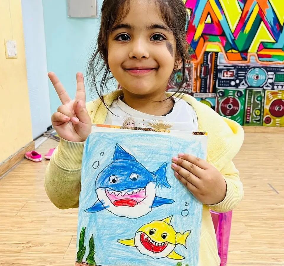 Look at this proud artist with her fantastic shark drawing! Our creative art sessions are all about letting kids explore their imagination and express themselves through color and paint, no matter how messy it gets.