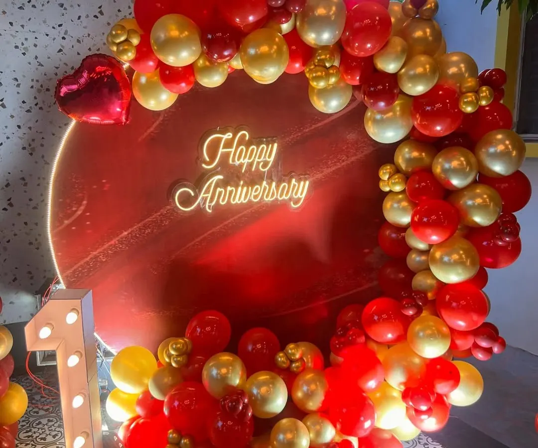 I design bold and beautiful backdrops to celebrate your special milestones. This first-anniversary setup features a vibrant red circular panel, a custom 'Happy Anniversary' neon sign, and a lush garland of red and gold balloons, complete with an illuminated number '1'.